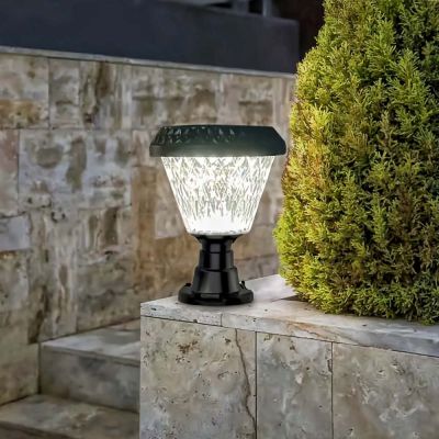 Elegant solar garden post light illuminating a stone corner wall at dusk beside garden steps and conifer tree.