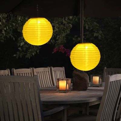 Two Yellow Solar Hanging Chinese Lanterns suspended from a garden umbrella above a candlelit outdoor table creating a romantic evening atmosphere