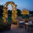 Solar Powered Fairy Lights Wrapped Around A Garden Arch And Trees At Dusk With Warm White Glow Over Patio Furniture