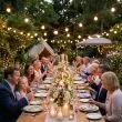 Festoon Lights With Warm White Bulbs Over A Long Garden Dinner Party Table With Candles And Flowers At Night